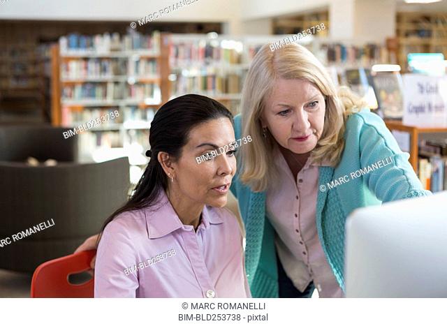 Older woman helping woman using computer in library