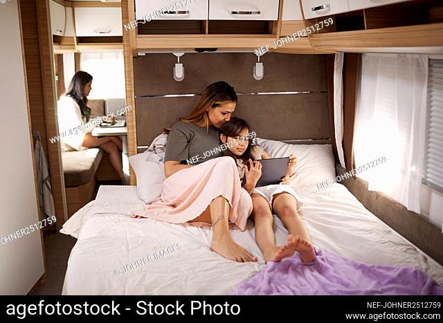 Mother and daughter sitting on bed in camper van