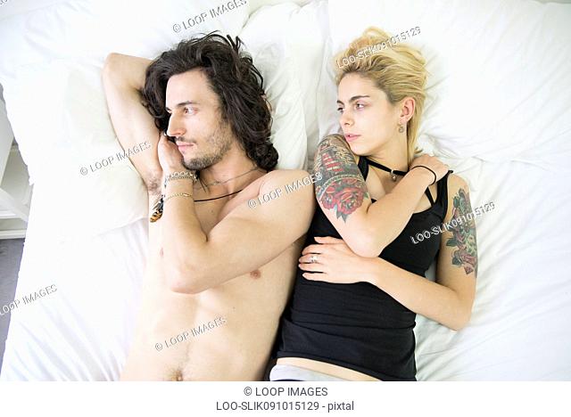 A young tattooed couple lying on a bed after an arguement