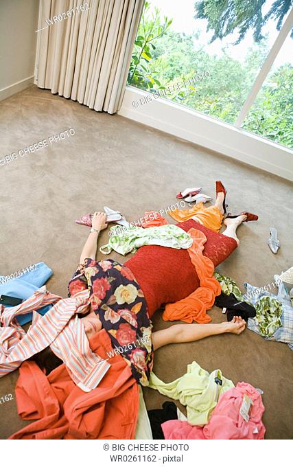 Woman on bedroom floor buried under clothing