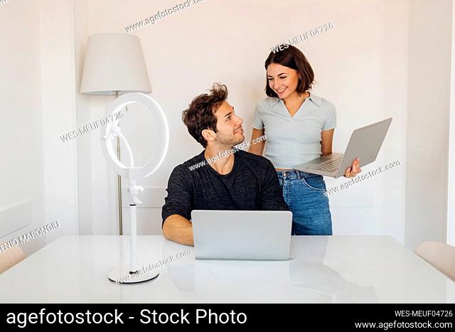 Smiling young couple with laptops looking at each other in home office