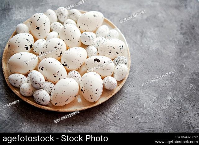 Composition of white traditional dotted Easter eggs in white ceramic plate placed on gray stone background. High angle shot