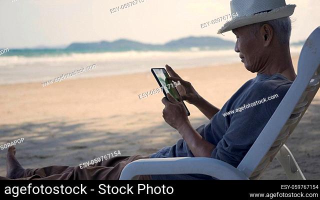 Senior man sitting on chairs enjoying time on beach travel vacation using tablet computer, Romantic elderly enjoy Travel summer vacation