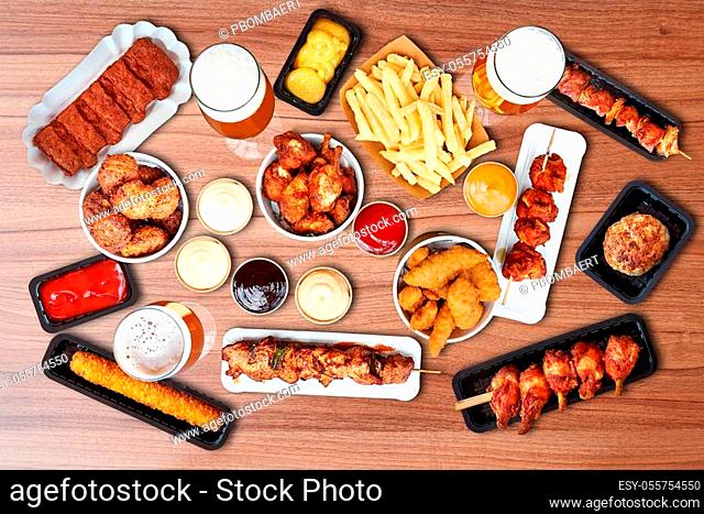 Composition of fried Fast food Snacks, sausage, french fries and beer on wooden table