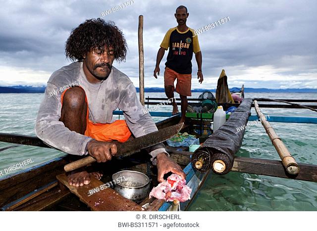 , Fisherman on outrigger boat carving up a fish, Indonesia, Western New Guinea, Cenderawasih Bay