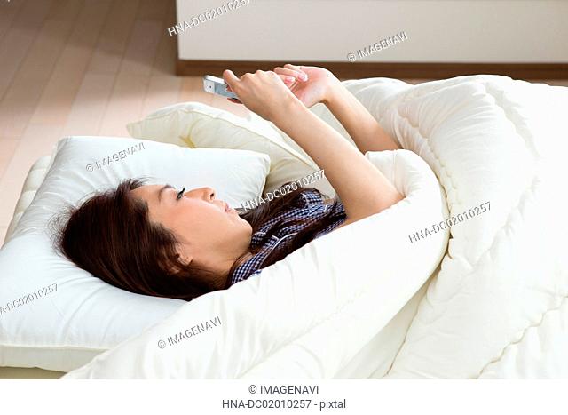 A woman seeing her Smartphone on the bed