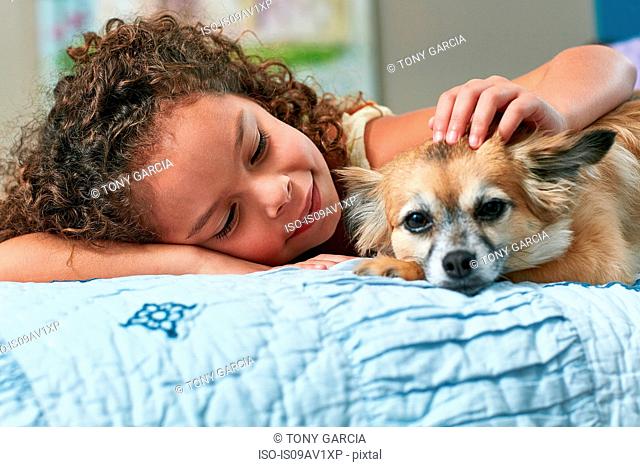 Girl lying on bed stroking dog
