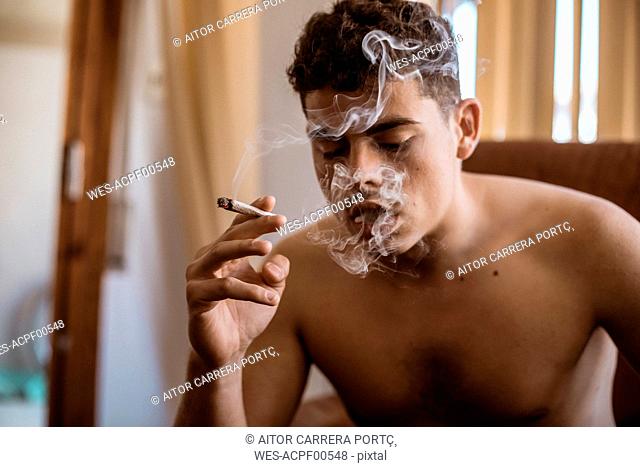Barechested man smoking a joint of marijuana