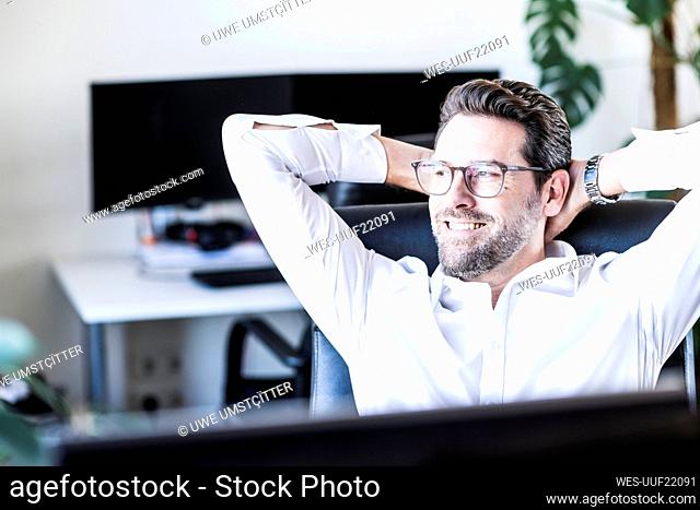 Male entrepreneur sitting with hands behind head at office
