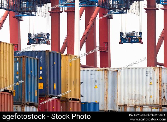 08 June 2022, Hamburg: The grabs of two container gantry cranes that are not in operation hang over stacks of containers at a container terminal in Waltershof