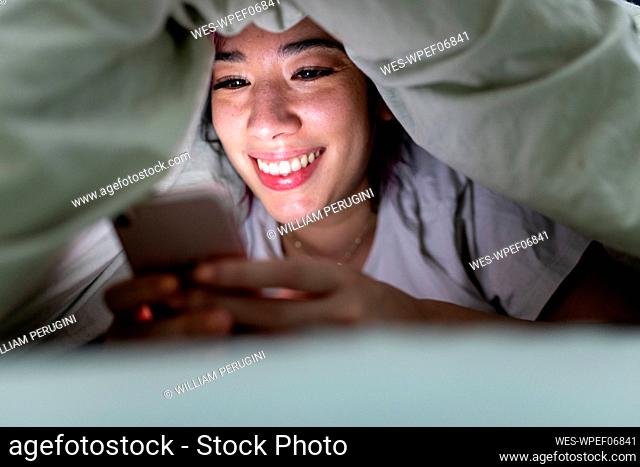 Happy woman using smart phone on bed at home