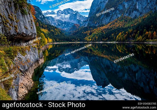 Sunny idyllic colorful autumn alpine view. Peaceful mountain lake with clear transparent water and reflections. Gosauseen or Vorderer Gosausee lake