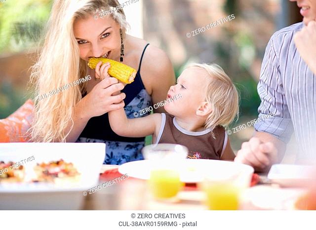 Toddler feeding mother corn outdoors