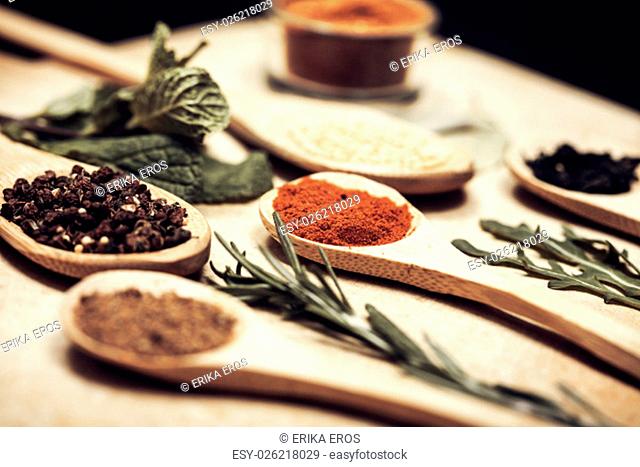 Various colorful spices on kitchen spoons over grunge wooden table