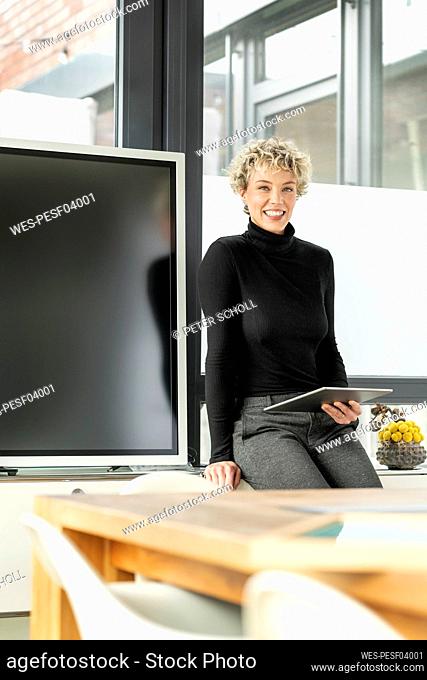 Happy businesswoman with tablet PC sitting in office