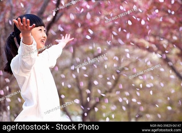 Happy young girl throwing cherry blossom petals in the air outside in a park in springtime