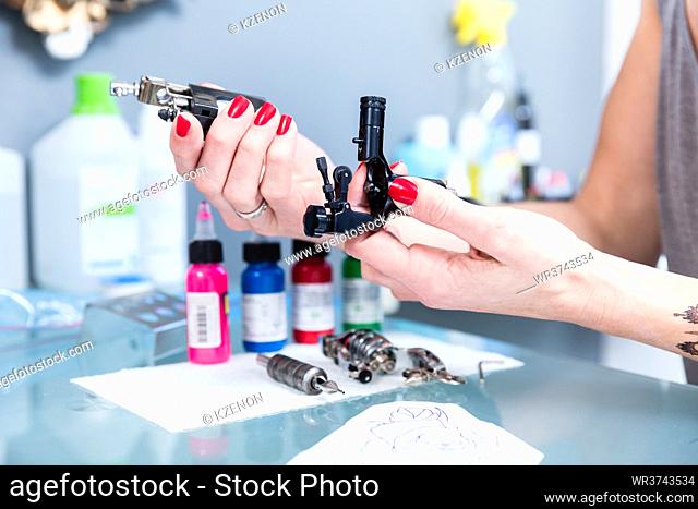 Close-up of the hands of a female artist preparing a professional tattoo machine before tattooing with colored inks in a modern studio