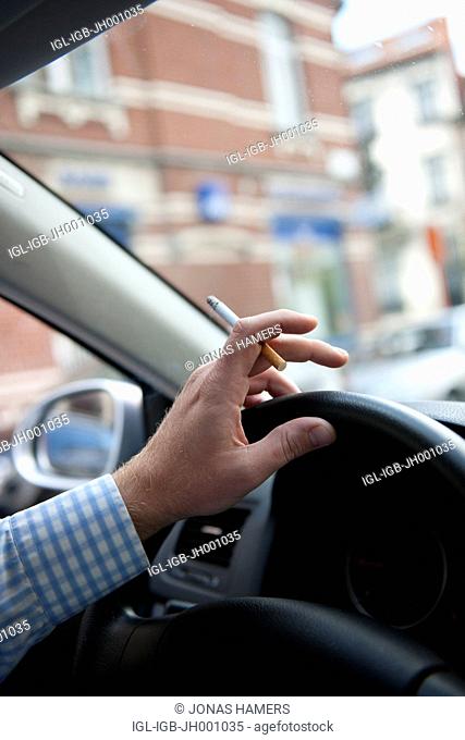 Man driving his car in the streets while smoking a cigarette