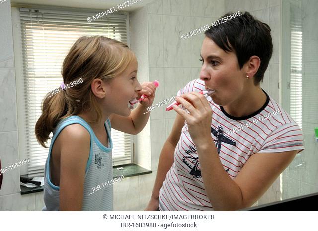 Woman, 35 years, and girl, 9 years, brushing their teeth