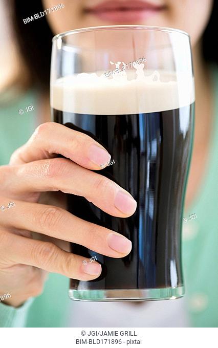 Mixed race woman drinking glass of dark beer