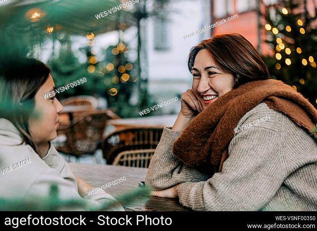 Happy mature woman talking with daughter sitting in sidewalk cafe