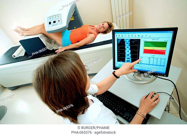 A doctor uses a bone densitometer to measure the optical density of the lower rachis backbone of female patient to diagnose osteoporosis