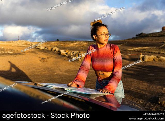Woman with map on car hood at sunset