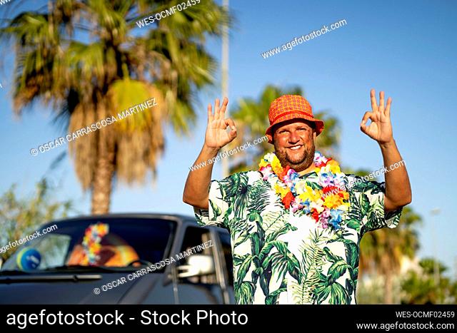 Smiling mature man wearing hat gesturing Ok signs on sunny day