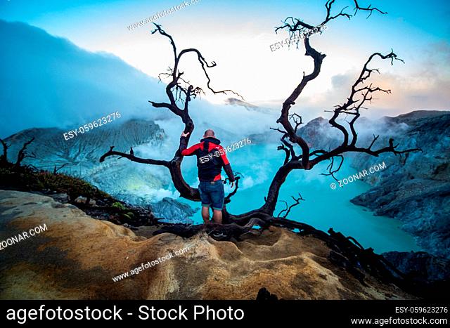 Man traveler on edge of crater Ijen volcano with colorful sky at morning. Beautiful Ijen volcano with acid lake and sulfur gas going from crater, Indonesia