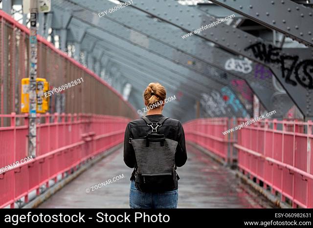 Solo casual woman walking the cycling lane on Williamsburg Bridge, Brooklyn, New York City, USA on overcast day