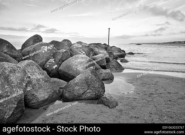 Stone groyne juts out into the water off the coast in Denmark. Black and white shot. Sunny day. Landscape photo by the sea