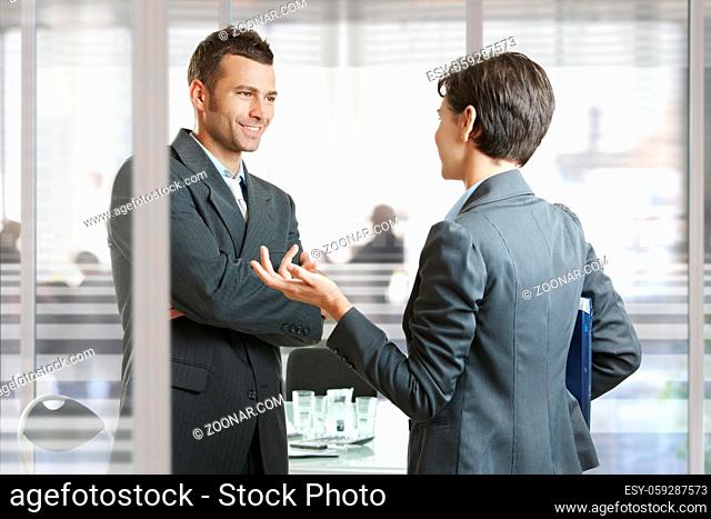 Businessman and businesswoman leaving meeting room, talking at the door, smiling