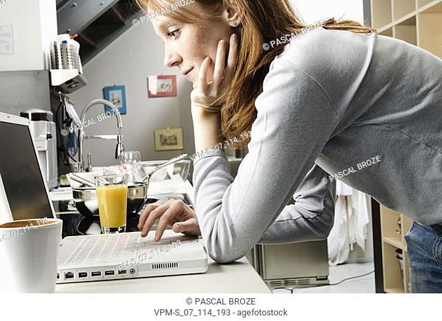 Side profile of a young woman using a laptop in the kitchen