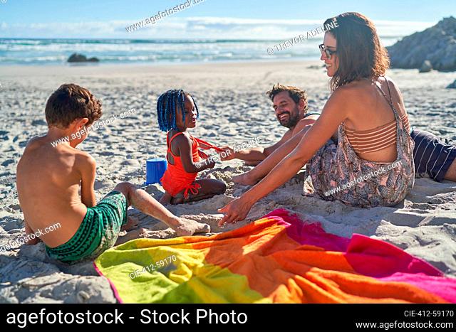 Family playing in sand on sunny summer beach