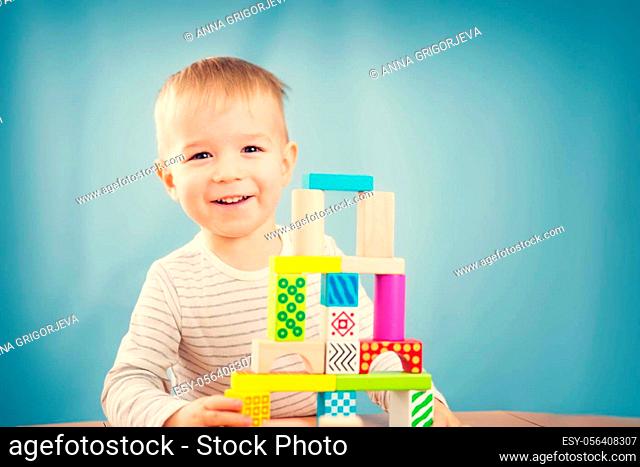 Portrait of a two years old child stacking wooden cubes. Pretty little boy on blue background