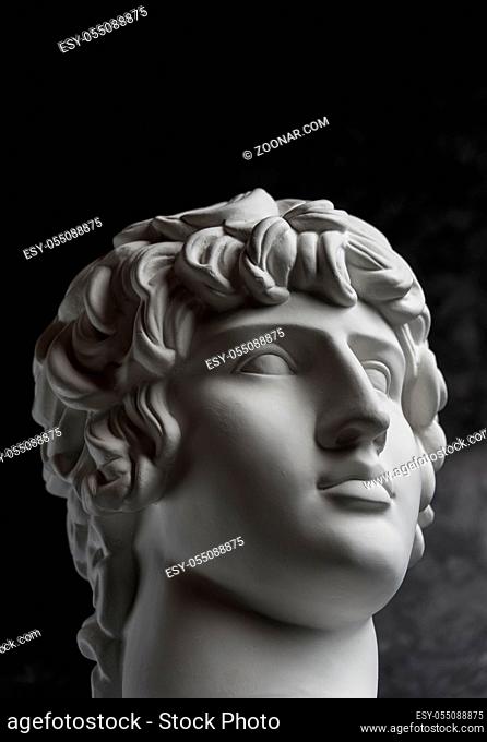 White gypsum copy of ancient statue of Antinous head for artists on a dark textured background. Plaster sculpture of man face