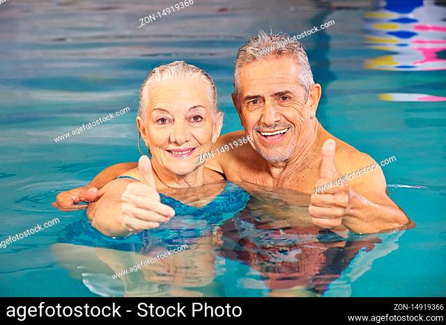 Glückliches Paar Senioren hält Daumen hoch im Schwimmbad im Wasser