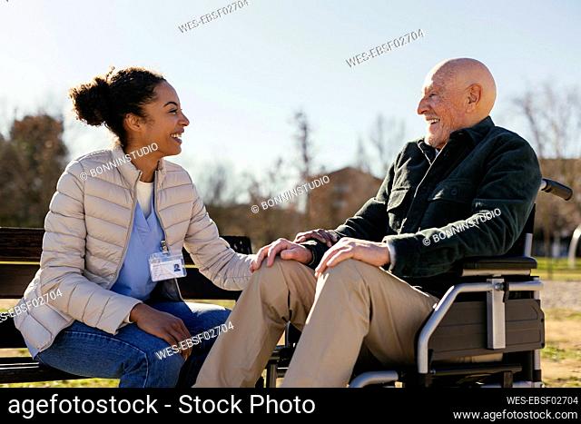Happy caretaker with senior man sitting on wheelchair in park