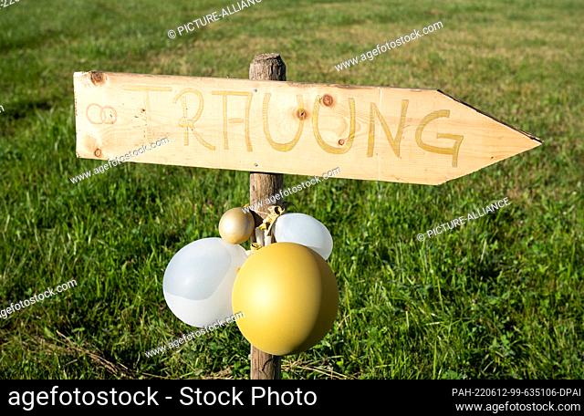12 June 2022, Baden-Wuerttemberg, Rottweil: A wooden sign with balloons attached to it points the way to a free wedding ceremony at the edge of a dirt road
