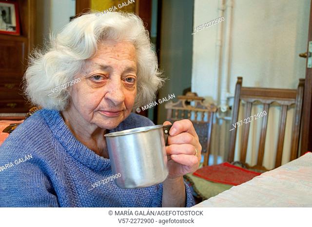 Old woman at home, drinking coffee and looking at the camera