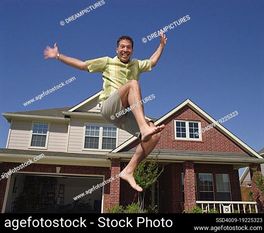 Middle aged man jumping in front of home, striking a pose mid air