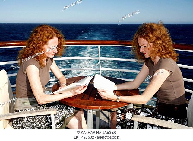 Two red-haired women (twins) sitting opposite each other reading books on the deck of cruise ship MS Europa (Hapag-Lloyd Kreuzfa