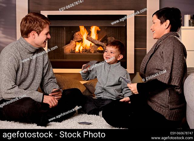 Young family with 4 years old kid playing card game at home in a cold winter day