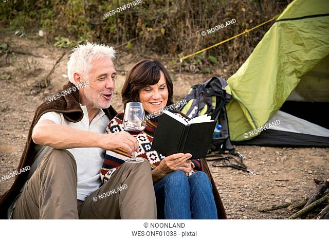 Happy senior couple with wine and book at a tent