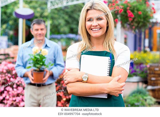 Woman holding a notepad while man holding a potted plant in the garden center