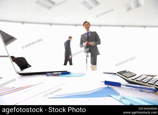 Business documents on office table with laptop and and calculator business diagram and men working in the background