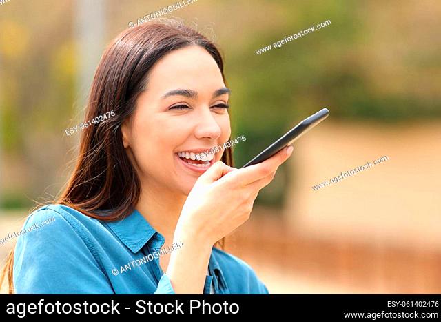 Happy woman dictating message using voice recognition in the street on smart phone