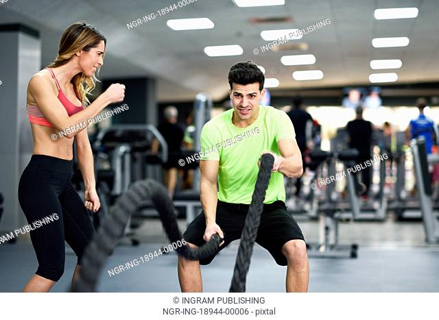 Female personal trainer motivating young man with battle ropes exercise in the fitness gym