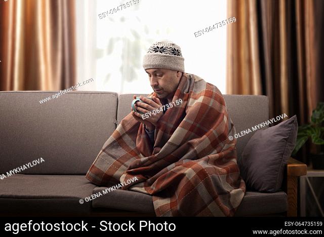 Middle age male model in hat and plaid hold coffee cup sitting on the sofa