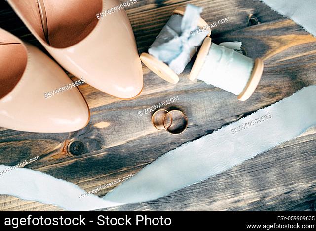 Gold wedding rings at the toes of the bride's beige shoes with a spool with a blue ribbon. High quality photo